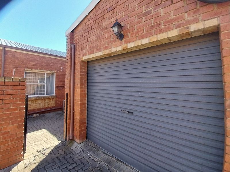 Exterior view of a brick garage featuring a roller door, paved driveway, and an adjacent window with security bars.