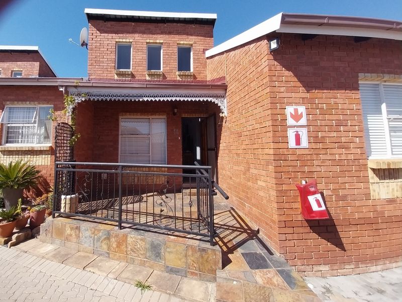 Front elevation of a retirement village unit featuring a brick facade, tiled porch entrance with wrought iron railing, and safety signage.