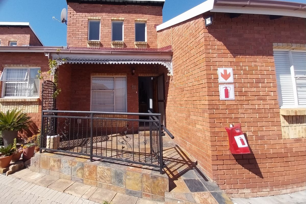 Front elevation of a retirement village unit featuring a brick facade, tiled porch entrance with wrought iron railing, and safety signage.