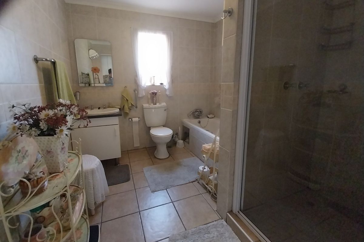 A functional bathroom featuring a vanity, toilet, bathtub, and separate shower enclosure with neutral wall and floor tiling.