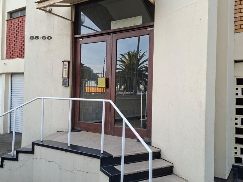 Front entrance of the apartment building featuring a glass double door, metal awning, and tiled steps with a metal handrail.