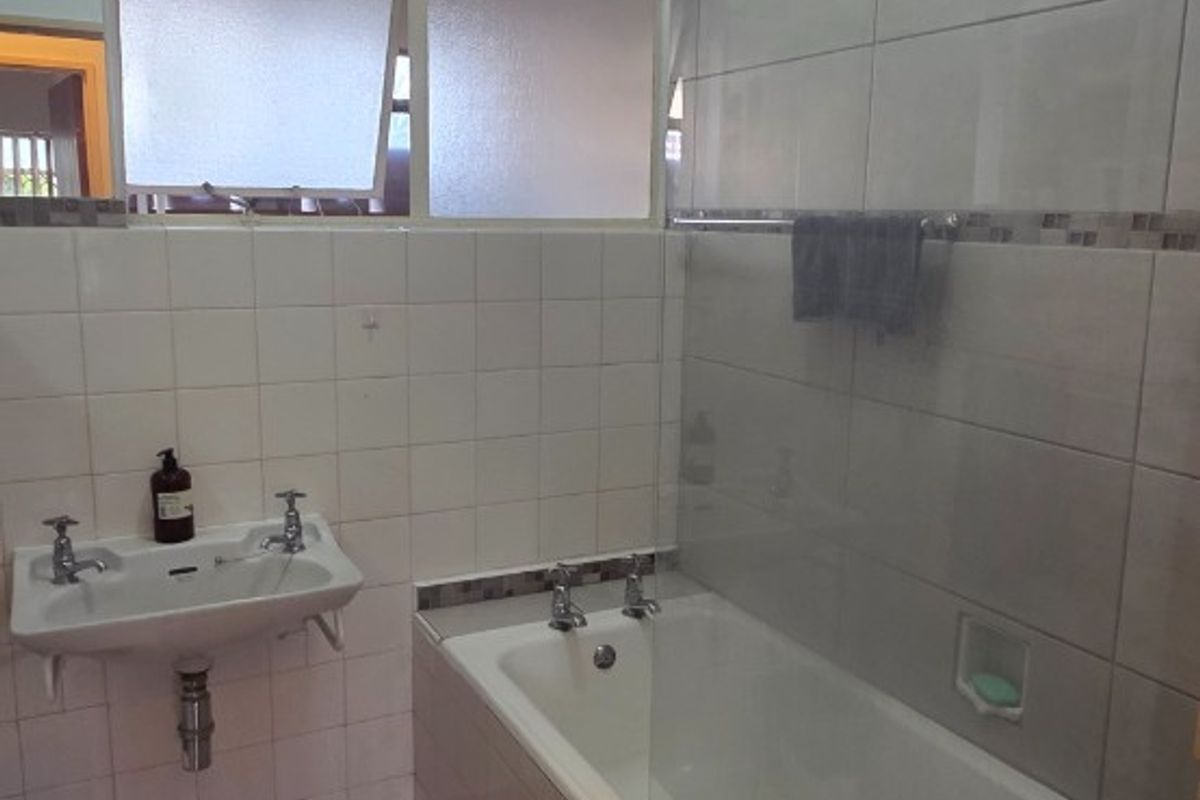 A functional bathroom featuring a wall-mounted basin, a bathtub with a glass shower screen, and neutral wall and floor tiling.