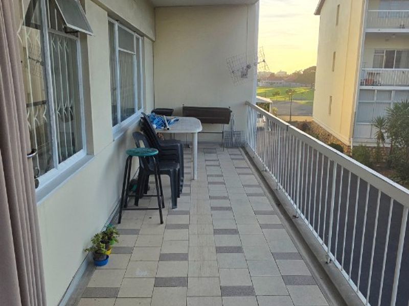 A covered balcony featuring tiled flooring and a metal balustrade, offering an outdoor space with views of the surrounding apartment complex.