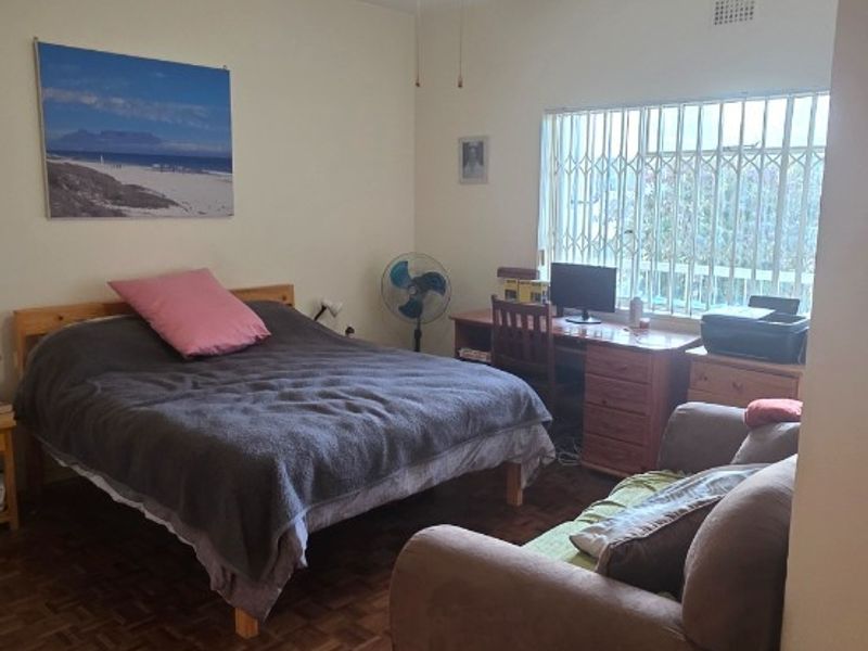 A bedroom featuring parquet flooring, a ceiling fan, and a window fitted with security bars.