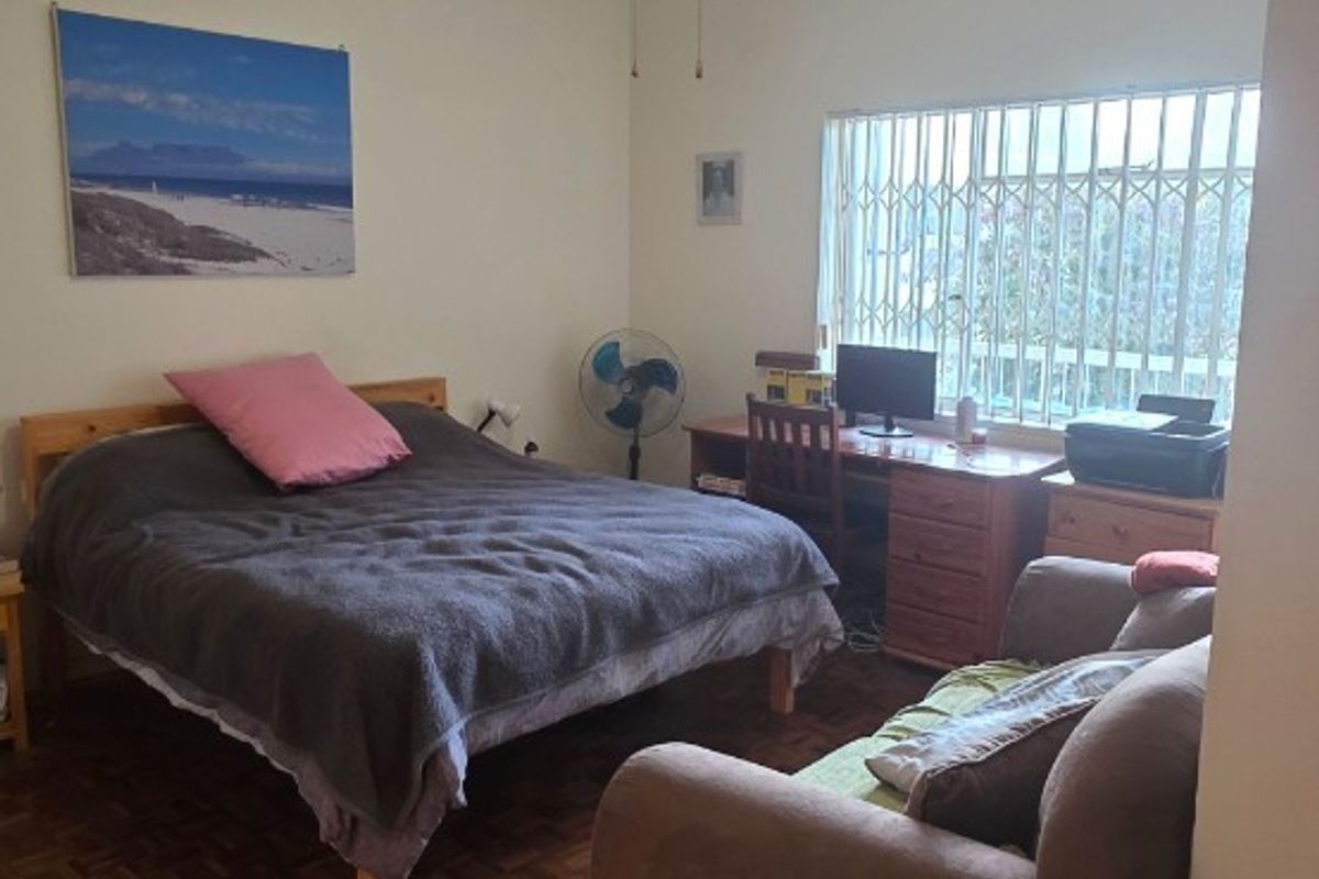 A bedroom featuring parquet flooring, a ceiling fan, and a window fitted with security bars.