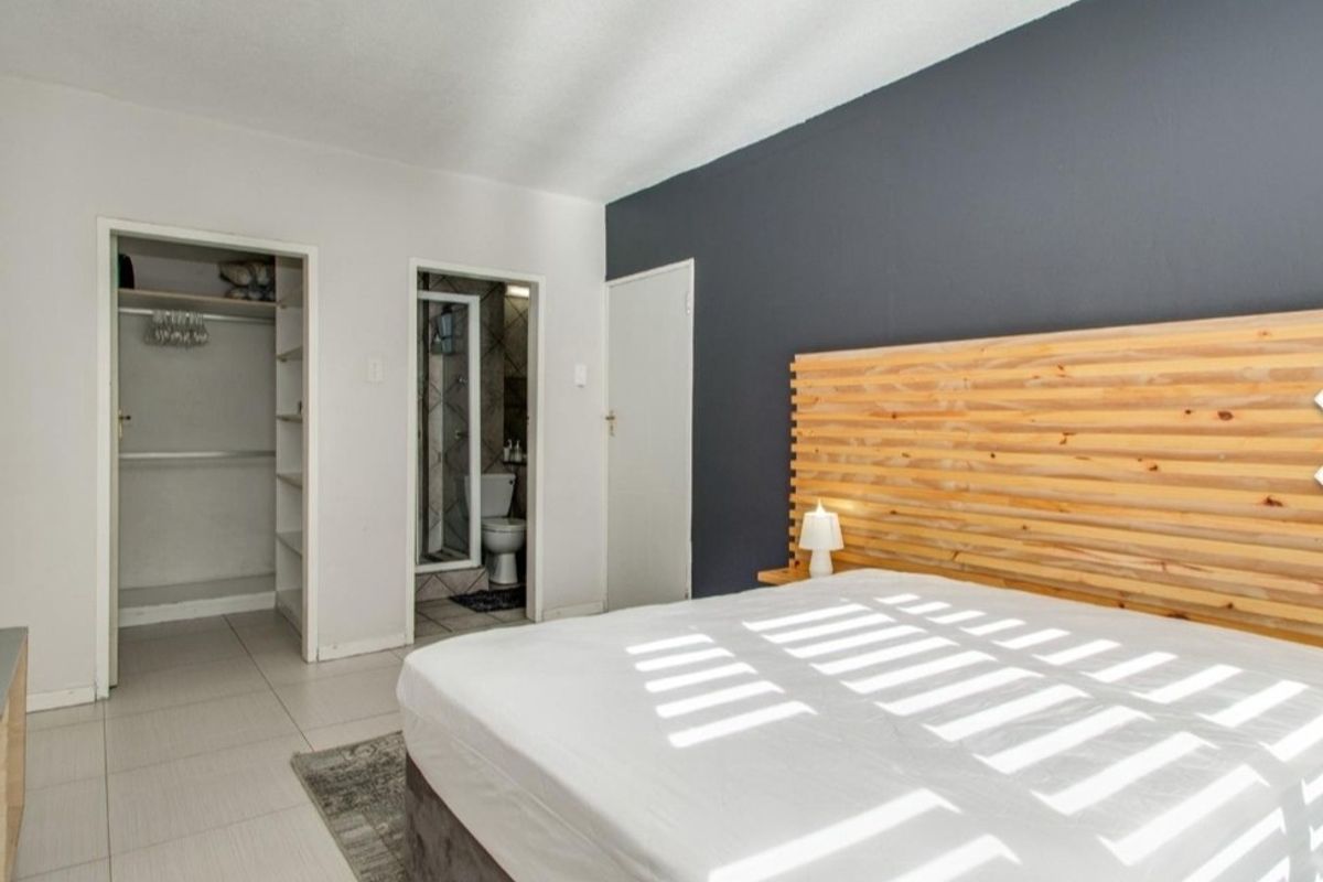 A well-maintained bedroom featuring tiled flooring, a built-in closet, and an en-suite bathroom with a modern dark accent wall.