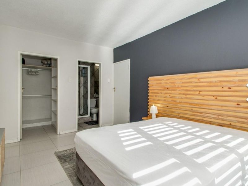 A well-maintained bedroom featuring tiled flooring, a built-in closet, and an en-suite bathroom with a modern dark accent wall.