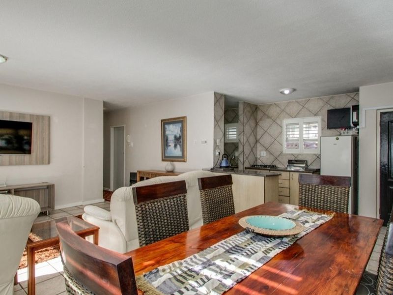 Open-plan living and dining area featuring tiled floors and a functional kitchen with built-in cabinetry, gas hob, and tiled backsplash.