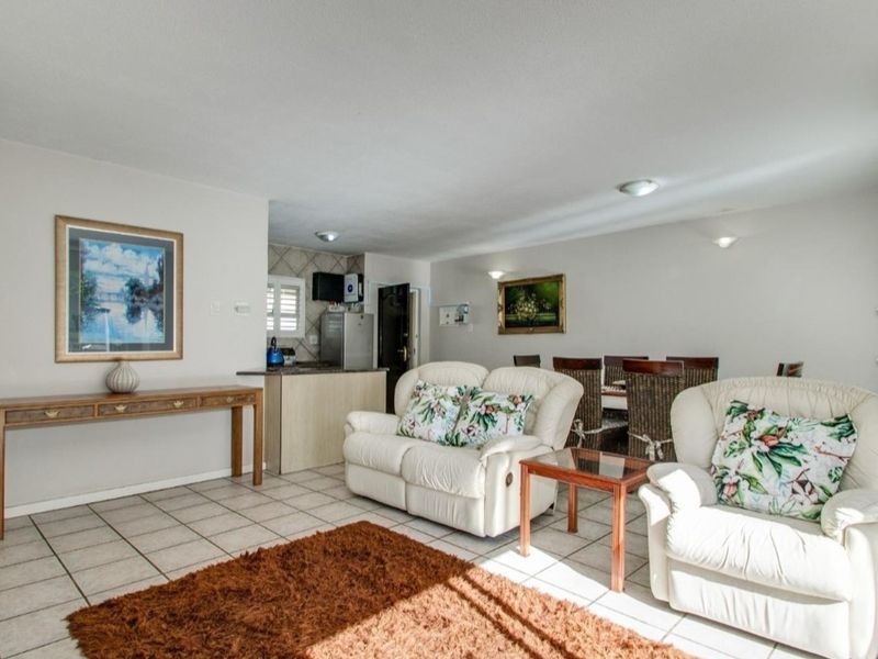 An open-plan living and dining area featuring tiled flooring, recessed lighting, and a compact kitchen space with built-in cabinetry.