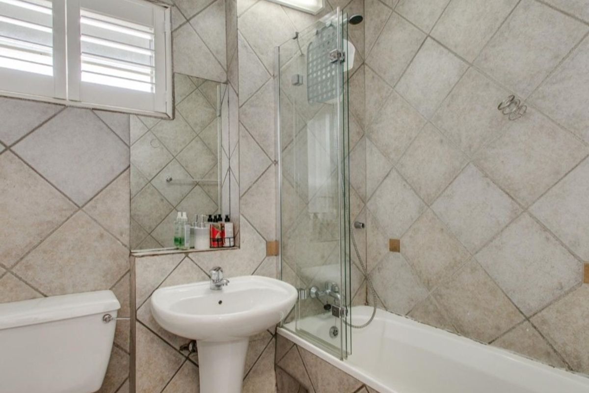 A functional bathroom featuring a pedestal basin, bathtub with a glass shower screen, and neutral ceramic wall tiling.