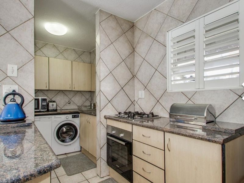 A functional kitchen featuring granite countertops, built-in oven, gas hob, and integrated laundry space with tiled finishes and shutter blinds.