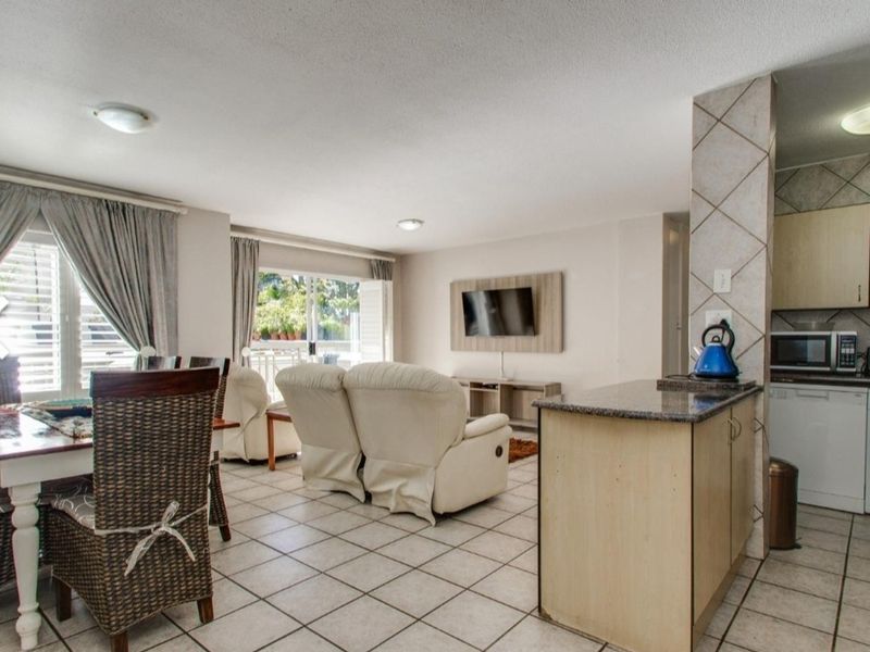Open-plan living and dining area featuring tiled flooring, a functional kitchen with granite countertops, and sliding door access to a balcony.