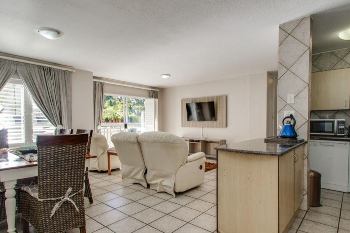Open-plan living and dining area featuring tiled flooring, a functional kitchen with granite countertops, and sliding door access to a balcony.