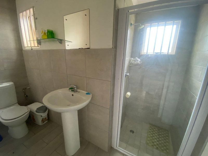 A functional bathroom featuring a pedestal basin, a separate shower enclosure, and a toilet, finished with neutral wall and floor tiles.