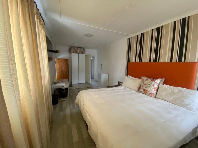 A functional bedroom featuring laminate flooring, a built-in wardrobe, and a neutral color palette with a feature wall.