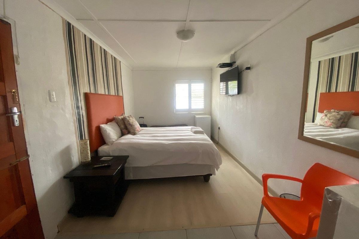 A compact bedroom featuring a louvered window, wall-mounted television, and neutral flooring, offering a functional and straightforward living space.