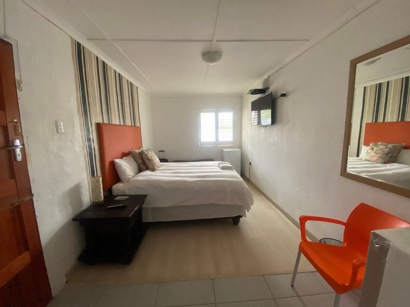A compact bedroom featuring a louvered window, wall-mounted television, and neutral flooring, offering a functional and straightforward living space.