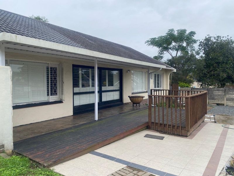 Rear exterior view featuring a covered timber deck, tiled patio area, and sliding glass doors with plantation shutters.