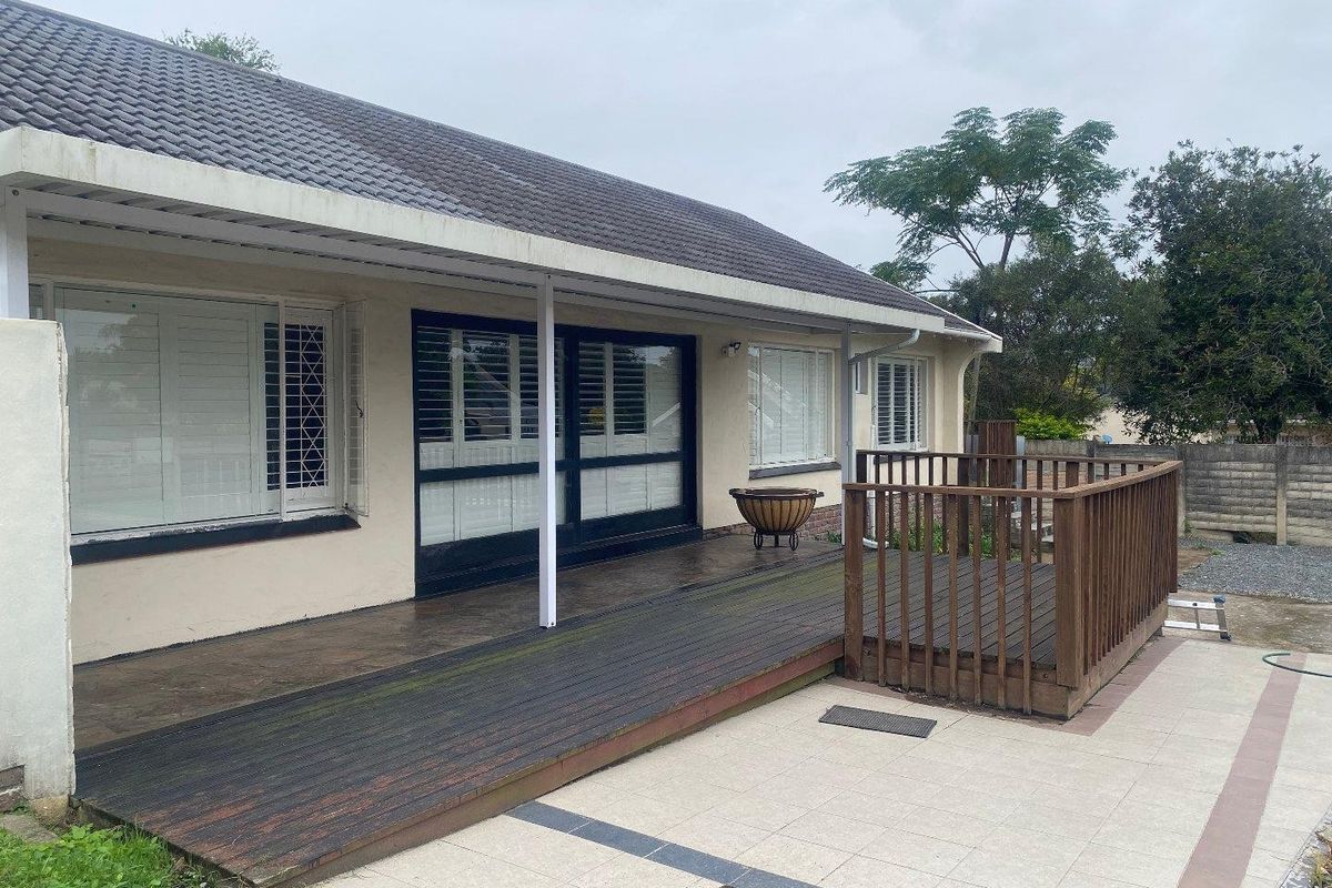 Rear exterior view featuring a covered timber deck, tiled patio area, and sliding glass doors with plantation shutters.