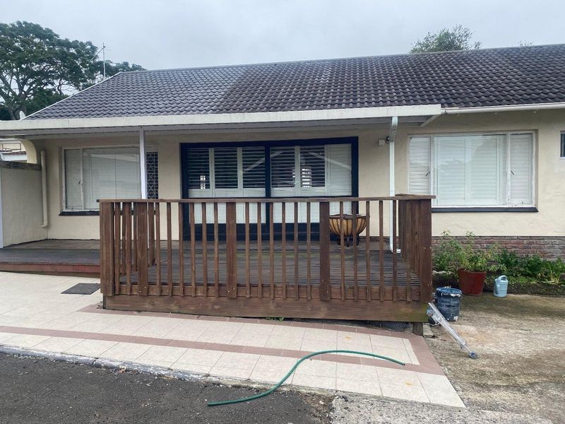 Rear exterior view featuring a raised timber deck, tiled patio area, and sliding glass doors with plantation shutters.