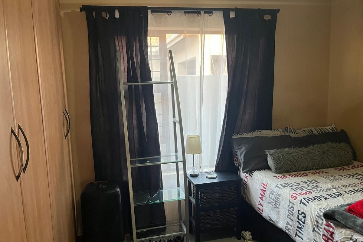 A bedroom featuring a built-in wardrobe and a window with curtains, providing natural light and storage space.