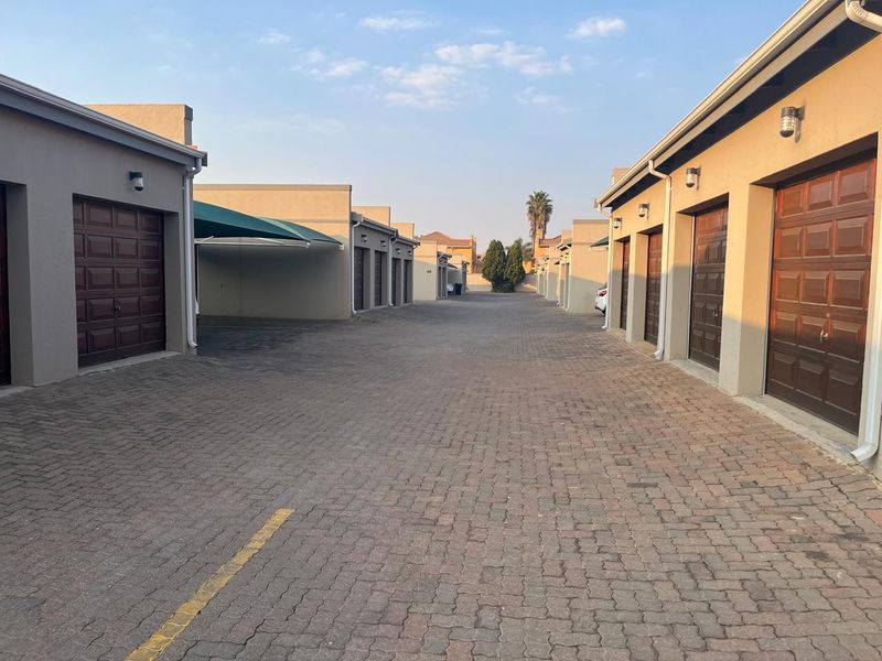 A view of a townhouse complex driveway featuring multiple garage units and a covered carport area with paved surfacing.