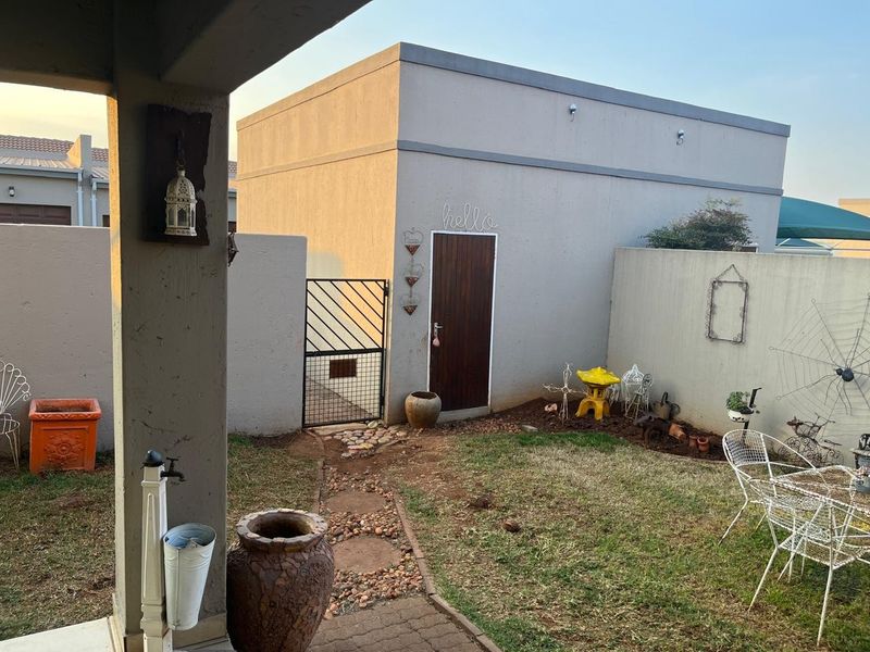 A private rear courtyard featuring a small lawn, paved pathway, boundary wall, and a covered patio area.