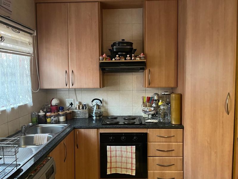 A functional kitchen featuring laminate cabinetry, a double bowl stainless steel sink, built-in oven, electric hob, and tiled splashback.
