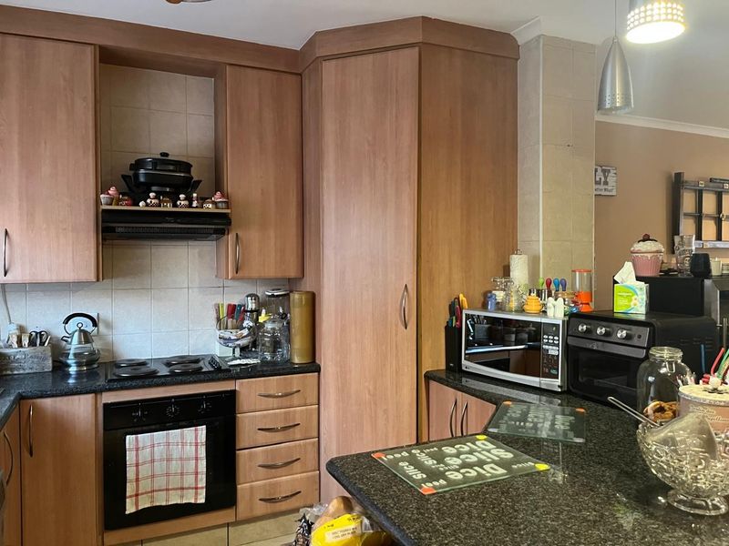 A functional kitchen featuring wood-look laminate cabinetry, dark granite countertops, a built-in oven, electric hob, and tiled backsplash with integrated lighting.