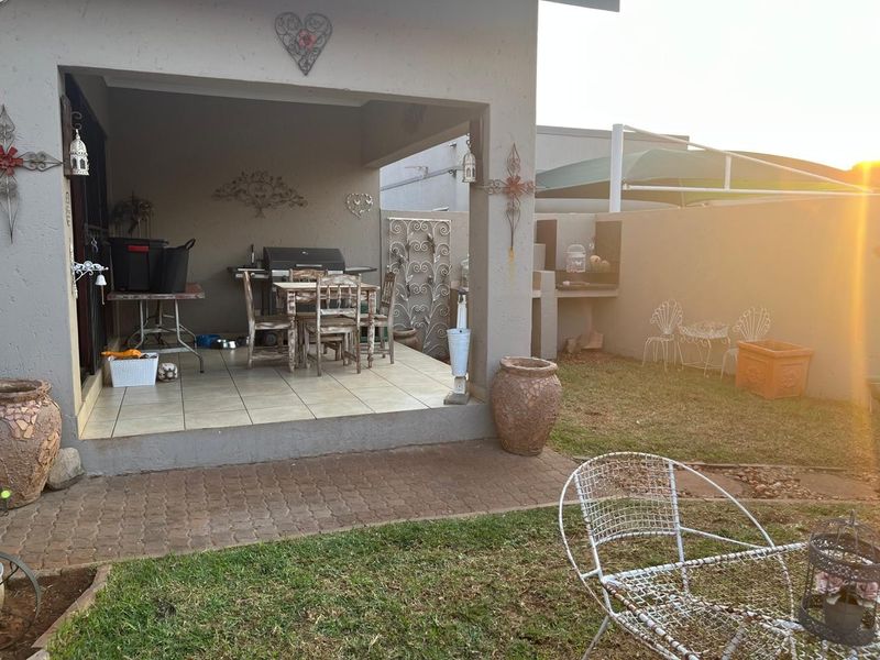 A covered patio area featuring tiled flooring and a built-in braai, overlooking a small private garden with paved pathways.