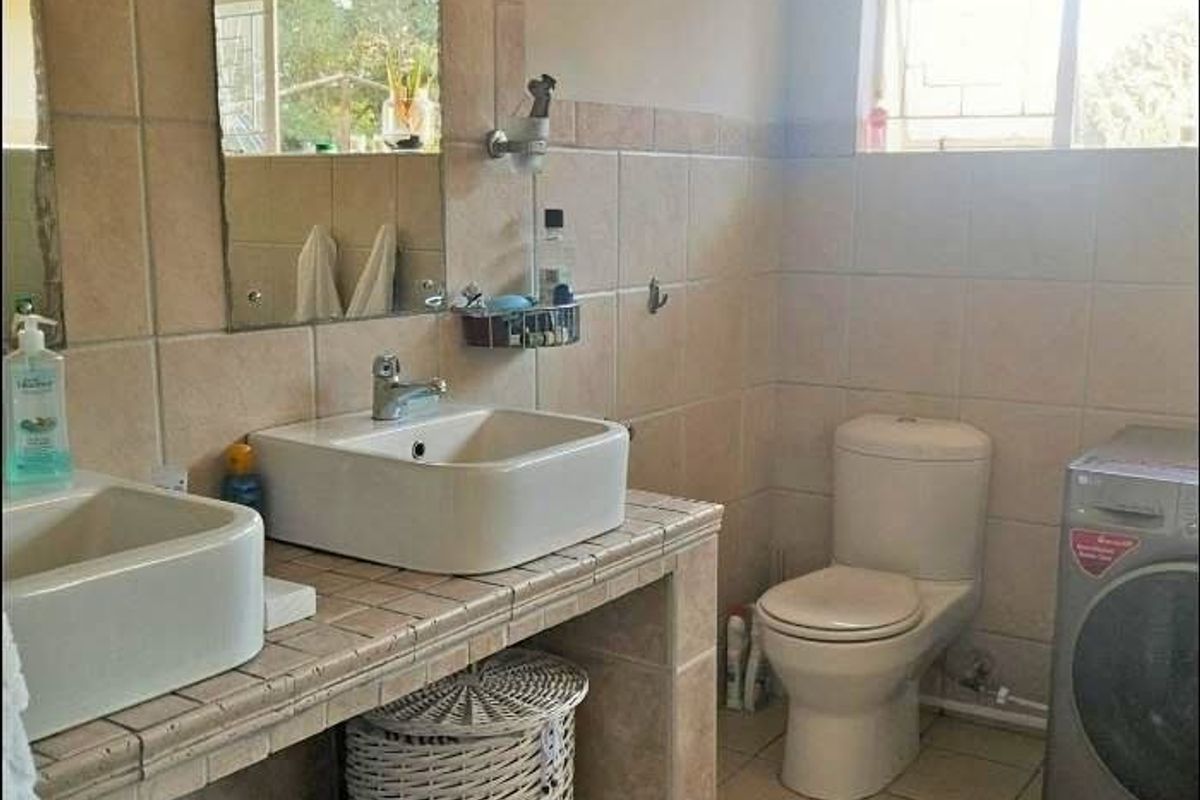 A functional bathroom featuring a tiled vanity with dual vessel sinks, chrome fixtures, and a standard ceramic toilet with wall-to-wall tiling.