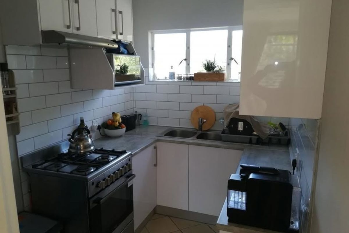 A compact, modern kitchen featuring white cabinetry, subway tile backsplash, gas stove with extractor, and double basin sink with laminate countertops.