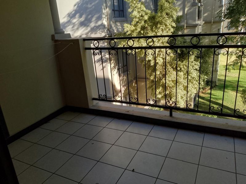 A private balcony featuring tiled flooring and a decorative wrought iron railing, overlooking the building's garden area.