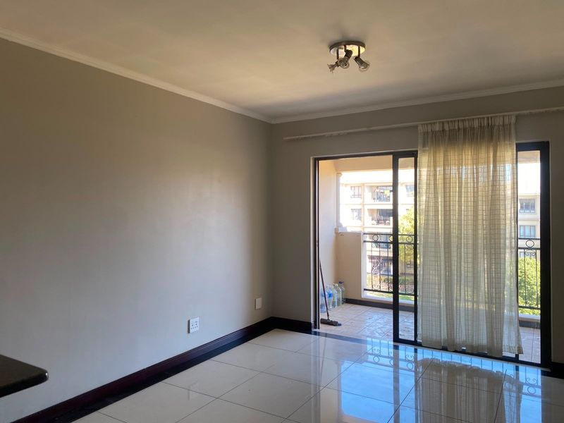 A bright, empty living room featuring tiled flooring and a sliding glass door that opens onto a private balcony.