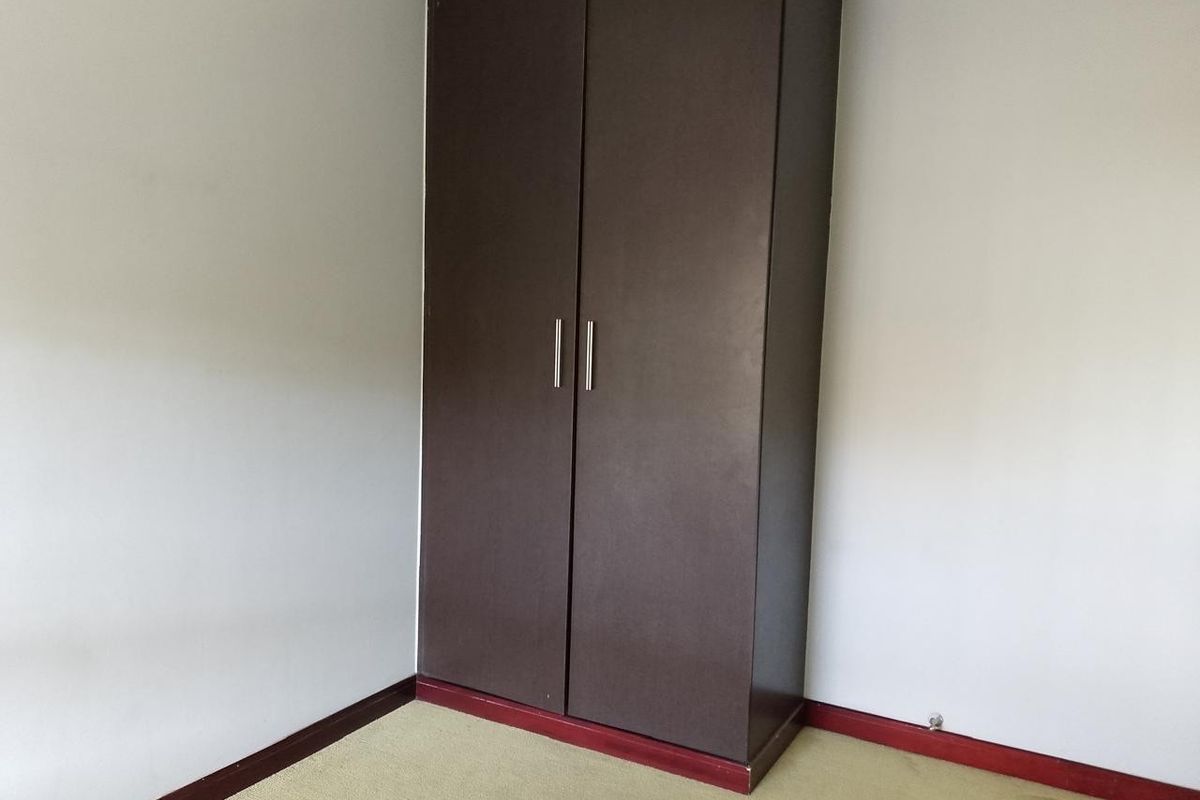 A simple bedroom featuring a dark brown built-in wardrobe and neutral carpeting.