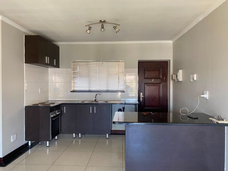 A functional kitchen featuring dark cabinetry, granite countertops, tiled flooring, and a breakfast bar, with an integrated stove and neutral wall finishes.