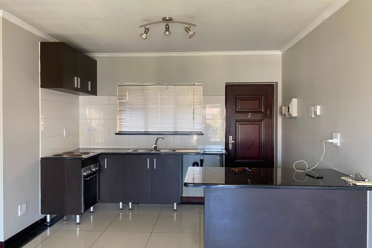 A functional kitchen featuring dark cabinetry, granite countertops, tiled flooring, and a breakfast bar, with an integrated stove and neutral wall finishes.