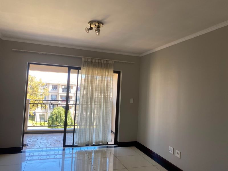A bright, empty living room featuring tiled floors, neutral walls, and a sliding glass door that opens onto a private balcony.