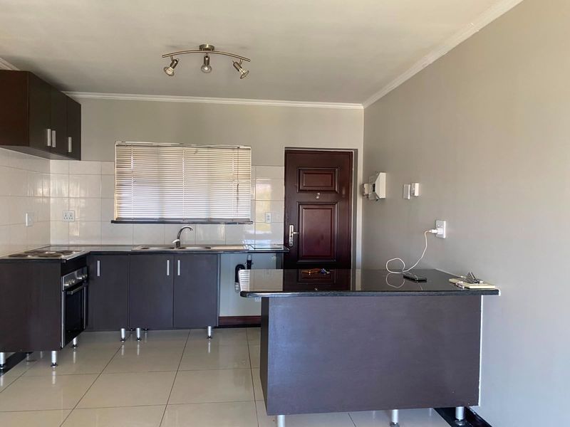 A clean, modern kitchen featuring dark cabinetry, granite countertops, built-in oven and hob, tiled flooring, and a functional breakfast bar area.