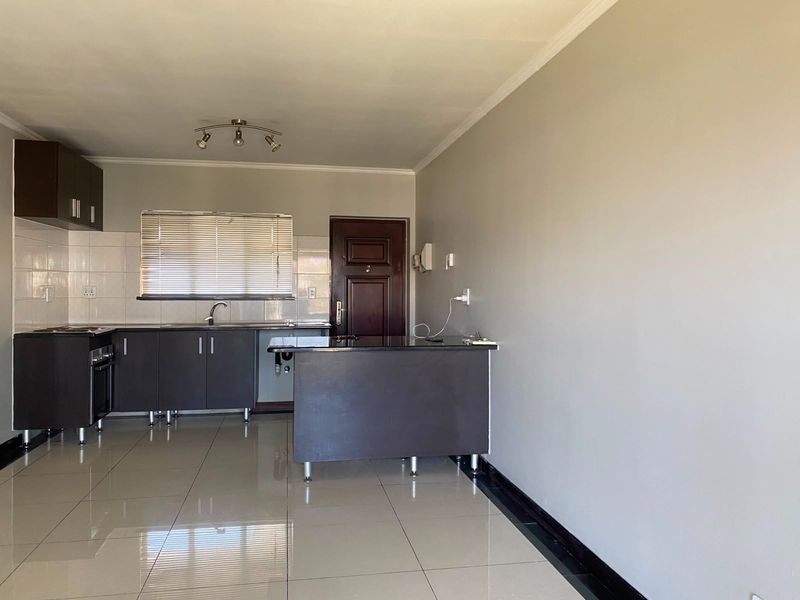 An open-plan kitchen area featuring dark cabinetry, a central island, tiled flooring, and a built-in oven, presenting a clean and functional space.