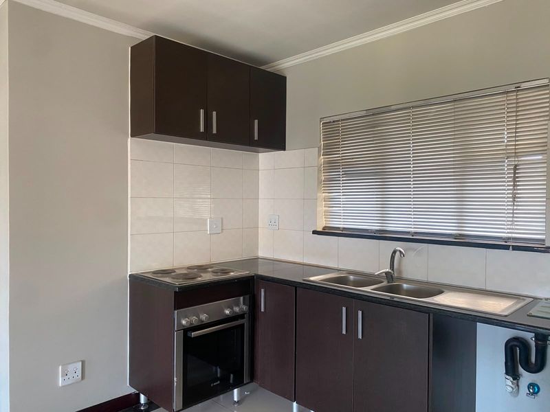 Compact kitchen featuring dark wood cabinetry, granite countertops, a built-in oven and hob, and a double sink with tiled backsplash.