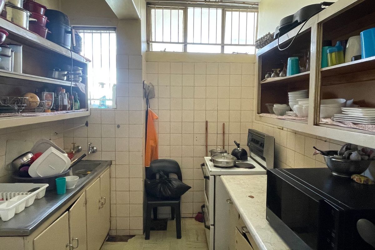 A compact, dated kitchen featuring tiled walls, built-in cabinetry, and a freestanding stove, offering significant potential for modernization and renovation.