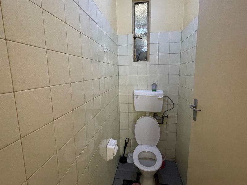 A compact, dated bathroom featuring tiled walls, a standard toilet, and an obscured glass window for privacy.