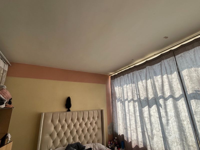 A bedroom featuring a large window with curtain tracks and recessed lighting, currently showing signs of wall surface wear and peeling paint.