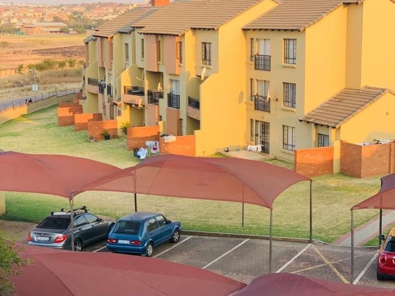 An elevated view of a residential apartment complex featuring yellow brick facades, tiled roofs, private balconies, and covered parking bays.