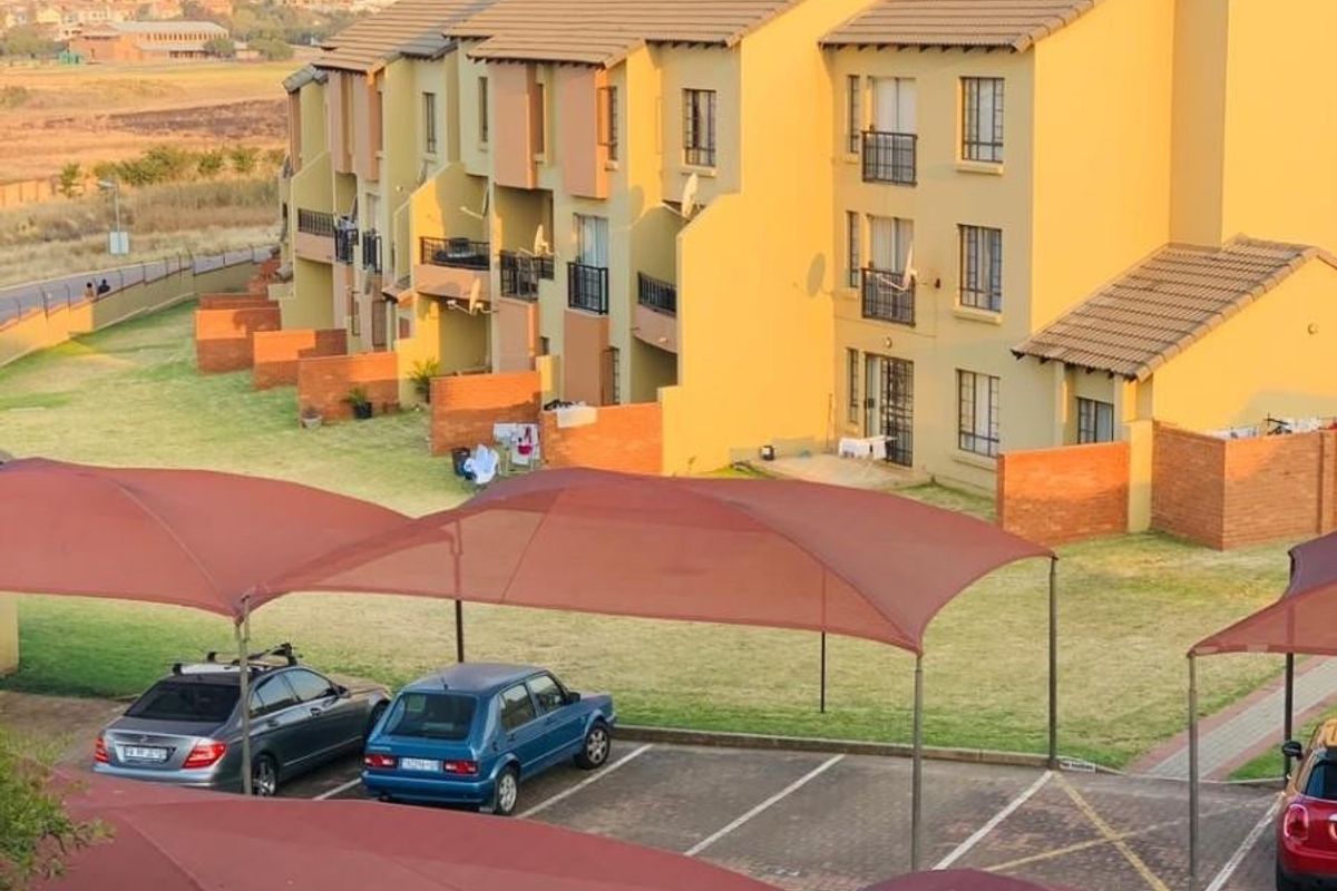 An elevated view of a residential apartment complex featuring yellow brick facades, tiled roofs, private balconies, and covered parking bays.