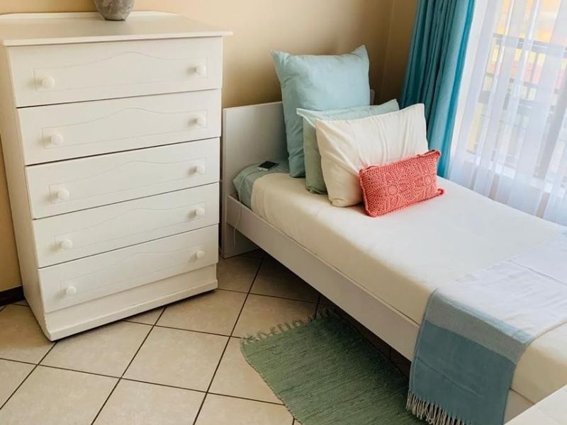 A compact bedroom featuring neutral tiled flooring and natural light through a window with installed curtain tracks.