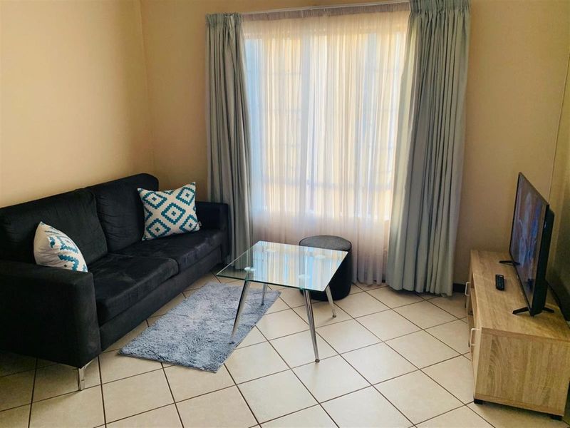 A functional living room featuring neutral tiled flooring and large window with installed curtain tracks, providing a bright and comfortable living space.