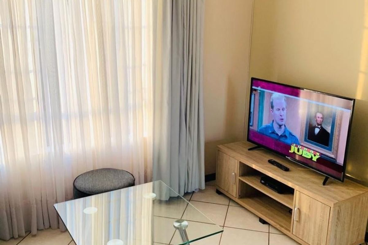 A living room area featuring neutral tiled flooring and large windows with installed curtain tracks, providing a bright and functional space.