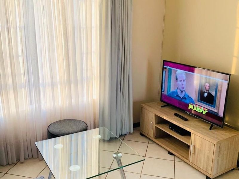 A living room area featuring neutral tiled flooring and large windows with installed curtain tracks, providing a bright and functional space.